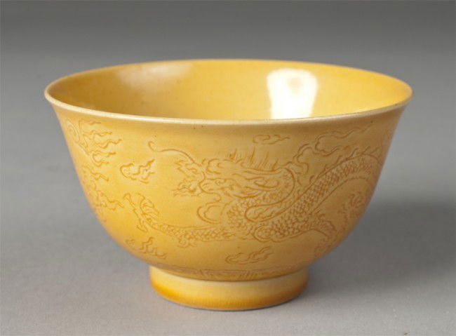 Chinese Yellow Molded Tea Cup: Footed tea cup finely molded to depict two 5-clawed dragons amid ruyi. Six character mark in underglaze blue for Great Qing Qianlong Production on underside. 2" H, 20th century.