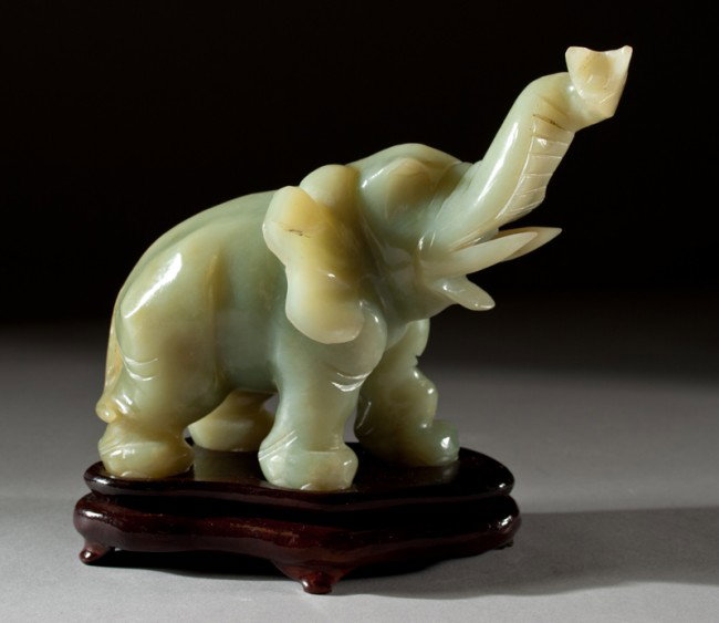 A Chinese Carved Jade Elephant: Finely carved to depict an elephant with tusk in upright position with matching hardwood stand. 7.5" L x 5.5" H, not including stand. Circa 20th century. Appraised in 1988 by Chicago Appraisers Associ
