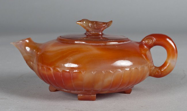 A Fine Chinese Carved Agate Tea Pot: Finley carved with a bird finial, the sides with carved ribs, all on four feet. 7" L x 3" H, large stone anomoles at top edge, visible in image #3 to the left of spout. Early 20th century.