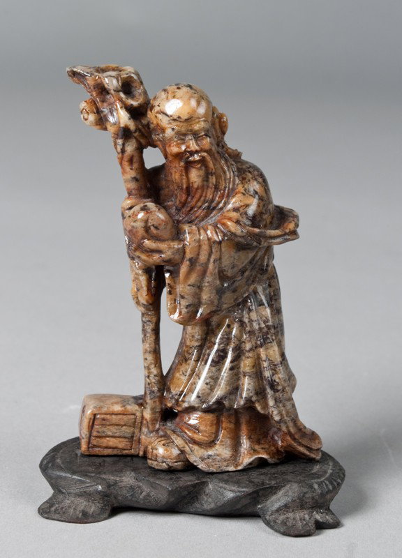 A Fine Chinese Carved Soapstone Elder Carving: Finely carved to depict an elder holding a staff and a peach alongside a chest. The stone a molted celadon color, mounted on a carved hardwood stand, and signed on underside of stone. 4" H, probably 1