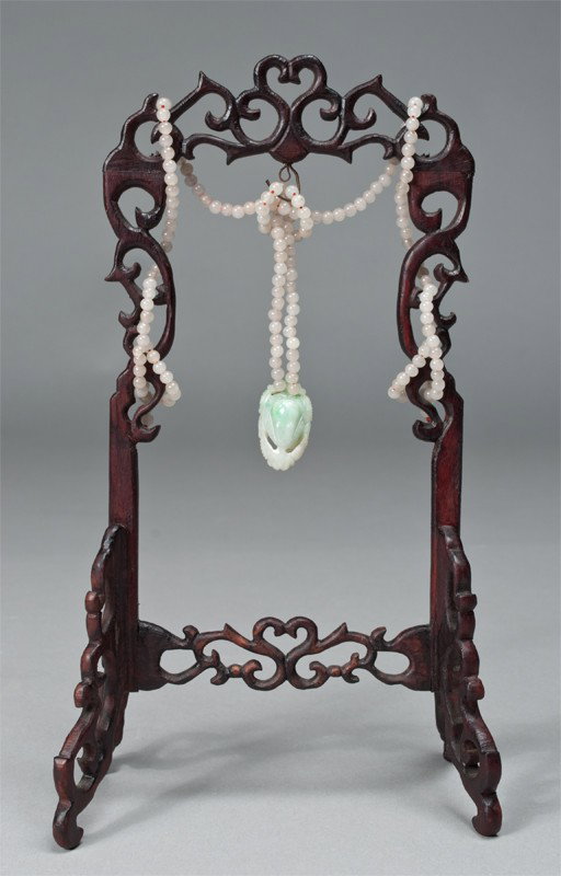 Chinese Jadeite Pendant On Carved Wood Stand: The jadeite pendant finely carved in the shape if a cicada, with a fine polish, hung from quartz beads, and displayed on a carved wood stand, pendant 1.25"L, stand 10"H, circa late 19th or early 20th 