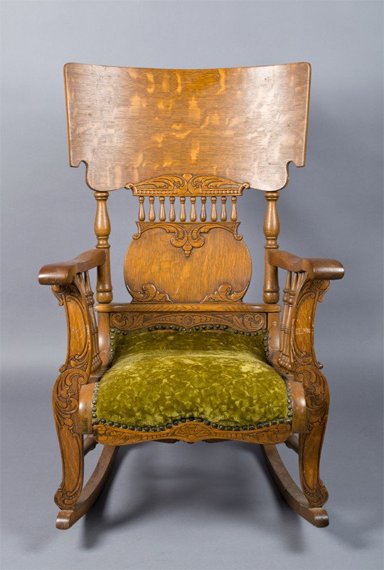 Antique Oak Wood Rocking Chair: Carved rocker with back splat, from arms and lower seat with carvings of scroll, fan and geometric designs, upholstered in green fabric. 40.5" H x 26" W x 32" D.