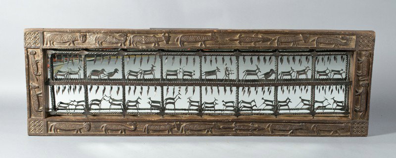 A Very Fine African Wood and Iron Mirror: A large African mirror with central hand wrought iron sculpture depicting animals and hanging tassels, framed in carved wood depicting animals with inset mirror behind ironwork. With mortise & tenon c
