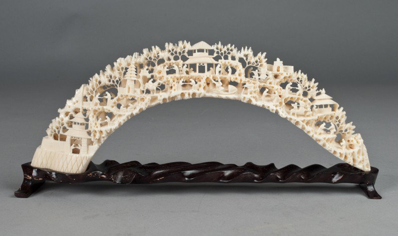 A Fine Chinese Carved Ivory Tusk On Stand: finely carved to depict figures in a village, mounted on a cared wood stand, 12.5"L, circa 20th century.