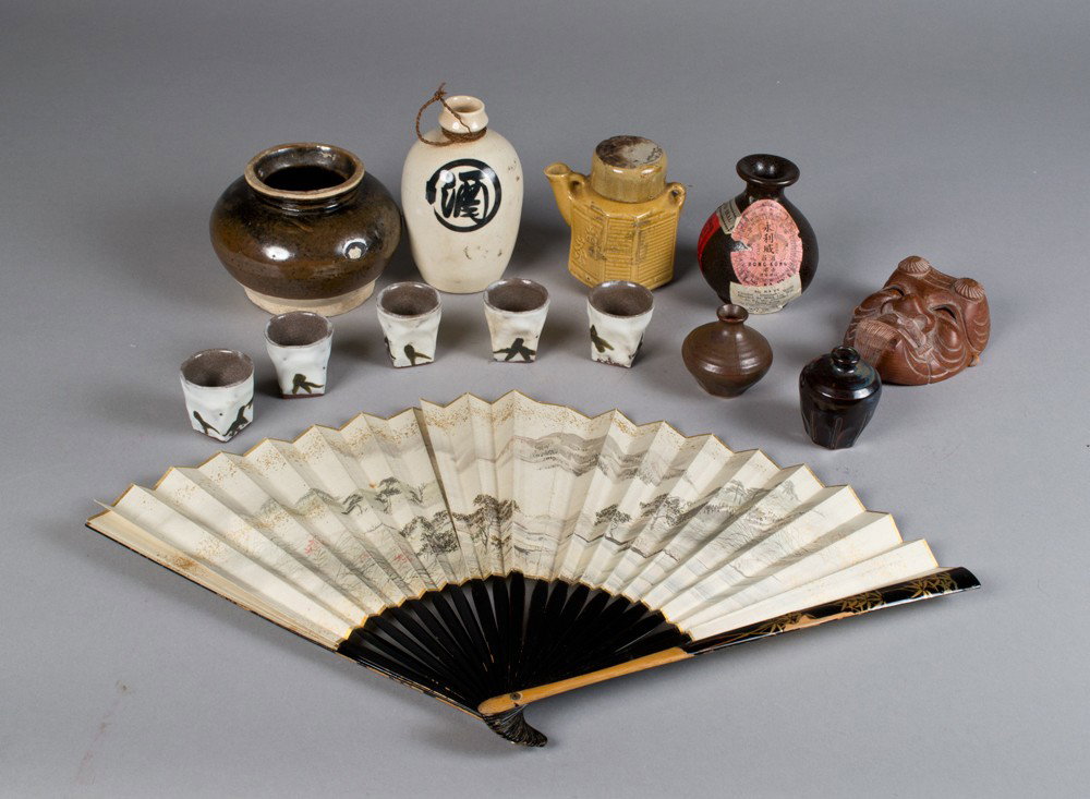 (13) Pcs. Chinese, Japanese Decorative Arts: To include Japanese sake bottle, five sake cups, a Chinese liquor jar, a Chinese brown glazed open jar, a tan glazed tea pot, a carved Japanese wood mask signed, a Japanese painted fan with lacquer st