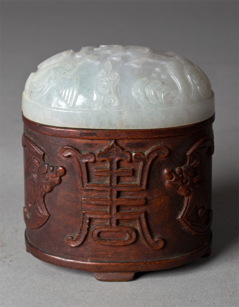 A Fine Chinese Huanghuali Wood & Jade Box: The box finely carved to depict bats and shou symbols on four ruyi shaped feet, with a fine burlwood grain, with a finely carved celadon jade top finely carved to depict a crane flying holding a preci