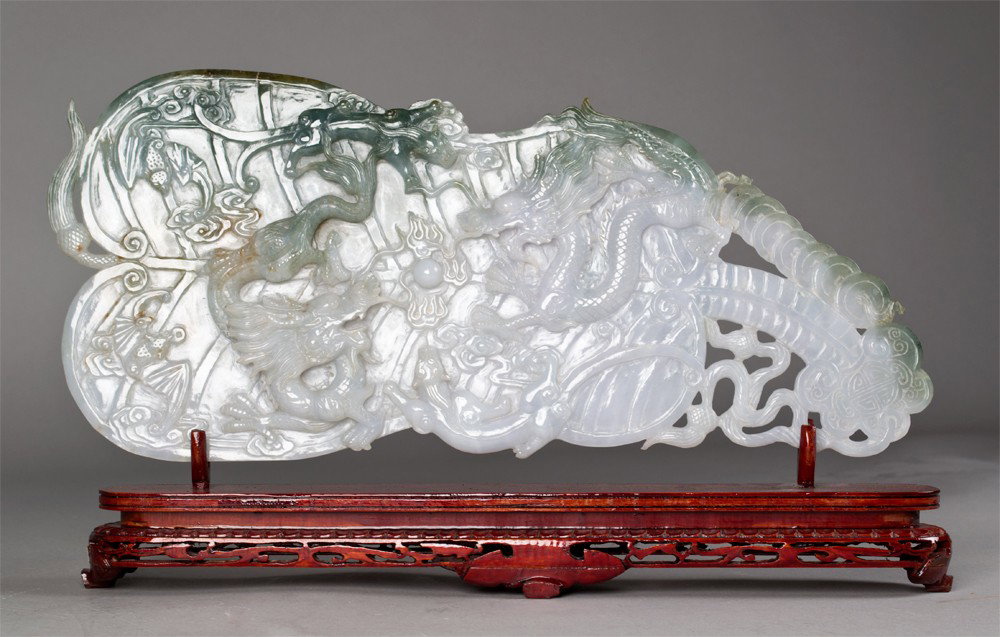 A Very Fine Chinese Carved Jade Fan: Very finely carved to depict a fan with raised dragons with a flaming pearl, chilongs, bats and coins. The reverse fan cabbage leaf form carvings, and rests on a carved wood stand. 7.25" H x 16" L, no