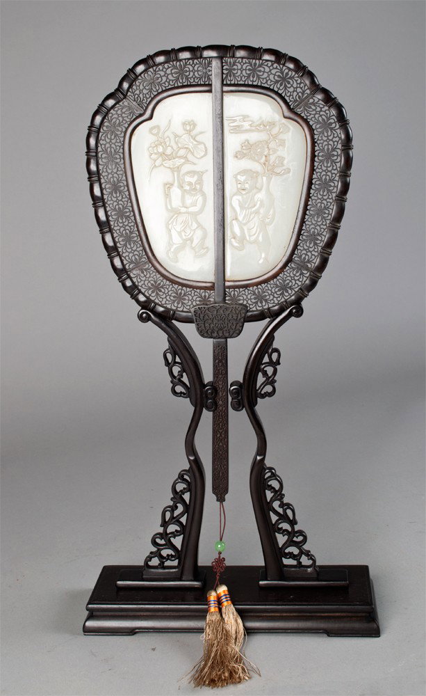 A Fine Chinese Jade and Hardwood Mounted Fan: Finely carved on one side to depict boys holding vases of flowers the reverse with four lines of calligraphy highlighted in gilt, jade measures 6.5"H X 5.5"W, total heights 19.5"H in fitted silk box c