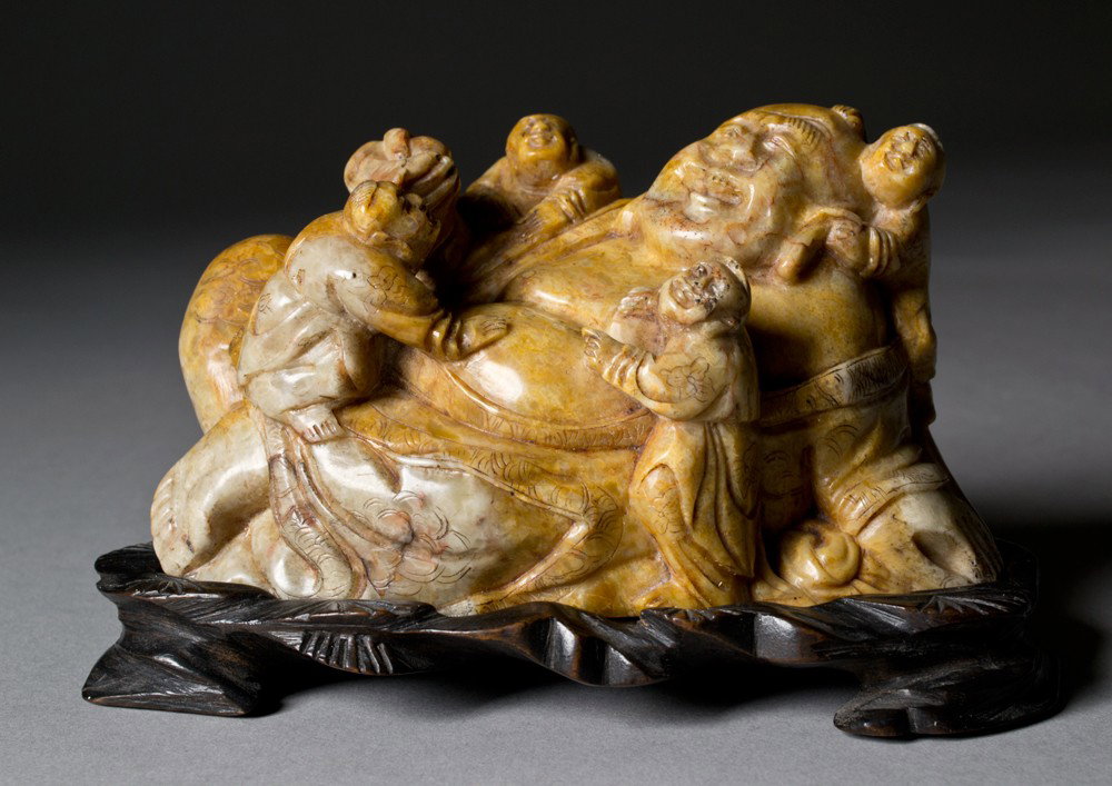 Chinese Carved Soapstone Figural Group: Depicting Maitreya Buddha with boys, very well carved with custom stand and a fine polish. 3.25" H x 5.50" L Appears to be an old red ink stamp to base, illegible to us. Base of soapstone and stand wi