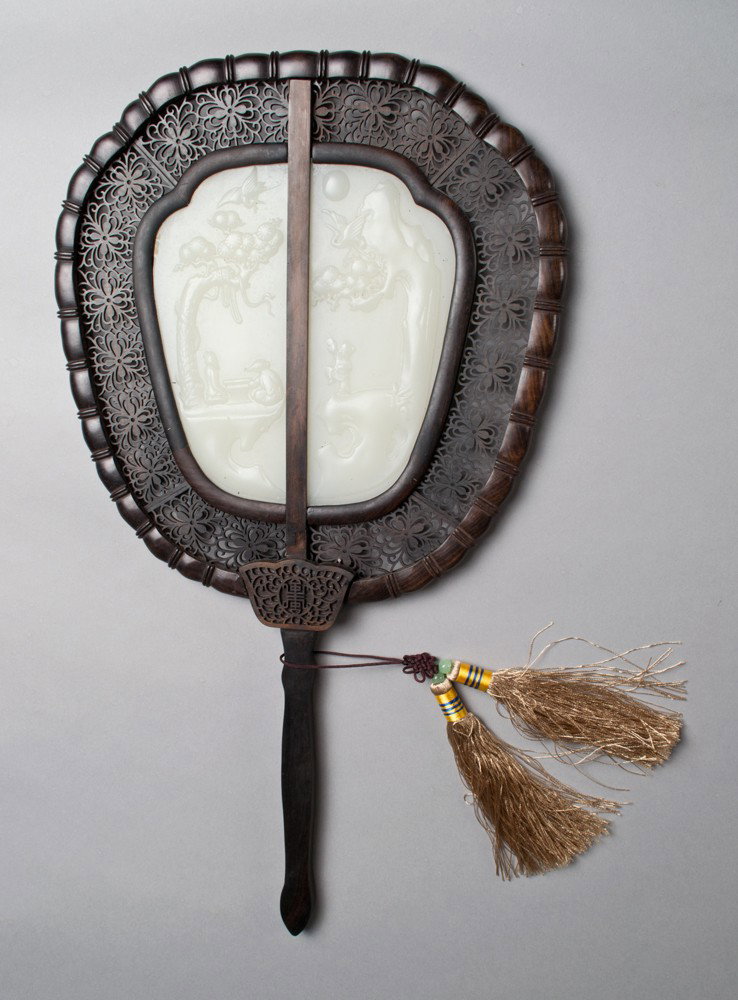 A Fine Chinese Jade and Hardwood Fan: The jade finely carved to depict a landscape scene with figures, trees and birds to one side. Mounted in an ornately carved hardwood frame with tassels, stand and custom fitted box. 15.25" L x 8 & 3/8