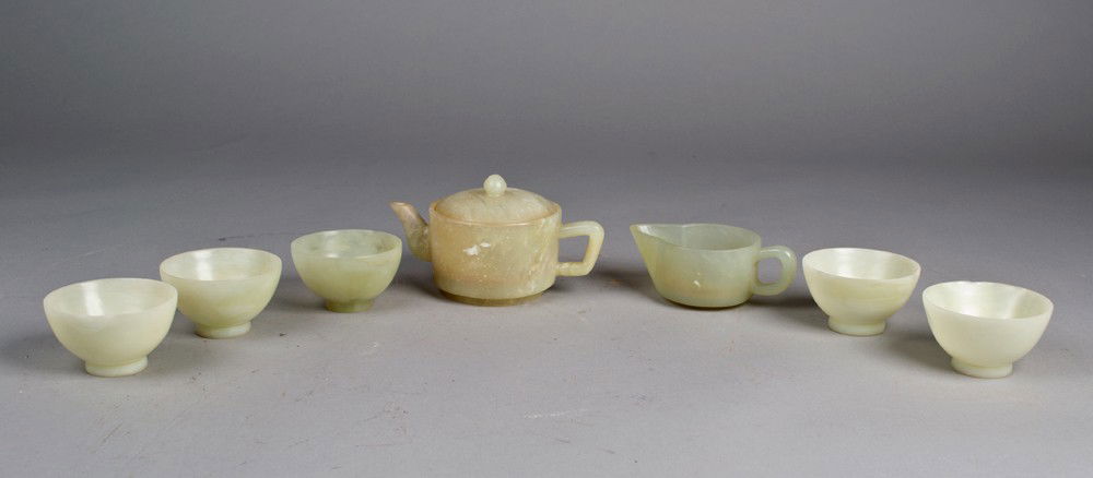 (8) Piece Chinese Carved Serpetine Jade Tea Set: To include tea pot, creamer, and five footed cups. The stone in light to medium celadon jade with fine polish. Largest 5.5" W x 3.25" H. Circa 19th/early 20th century.