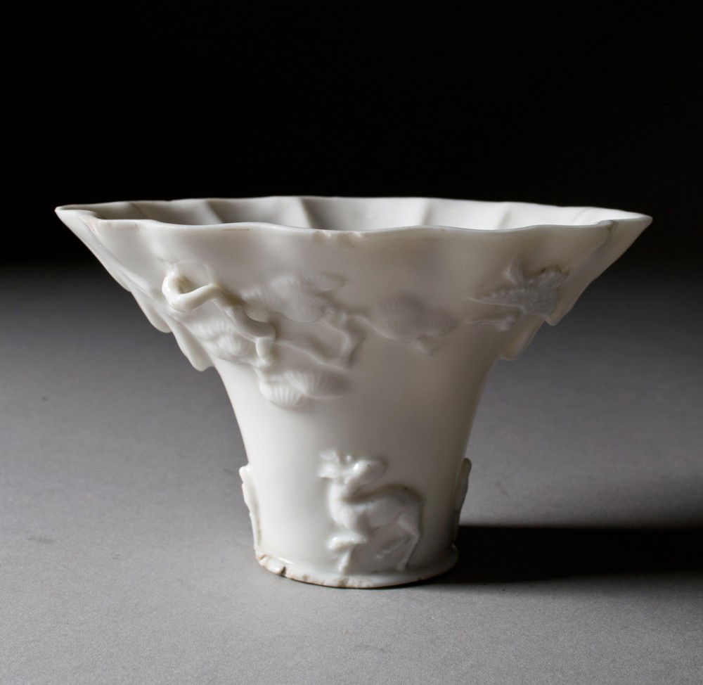 Chinese Blanc de Chine Libation Cup: Finely molded to depict deer. Foo dogs and cranes amongst a landscape the form simulating a rhino horn caving of the same period, 3.5"H X 6"W rim with small flakes circa 18th century.