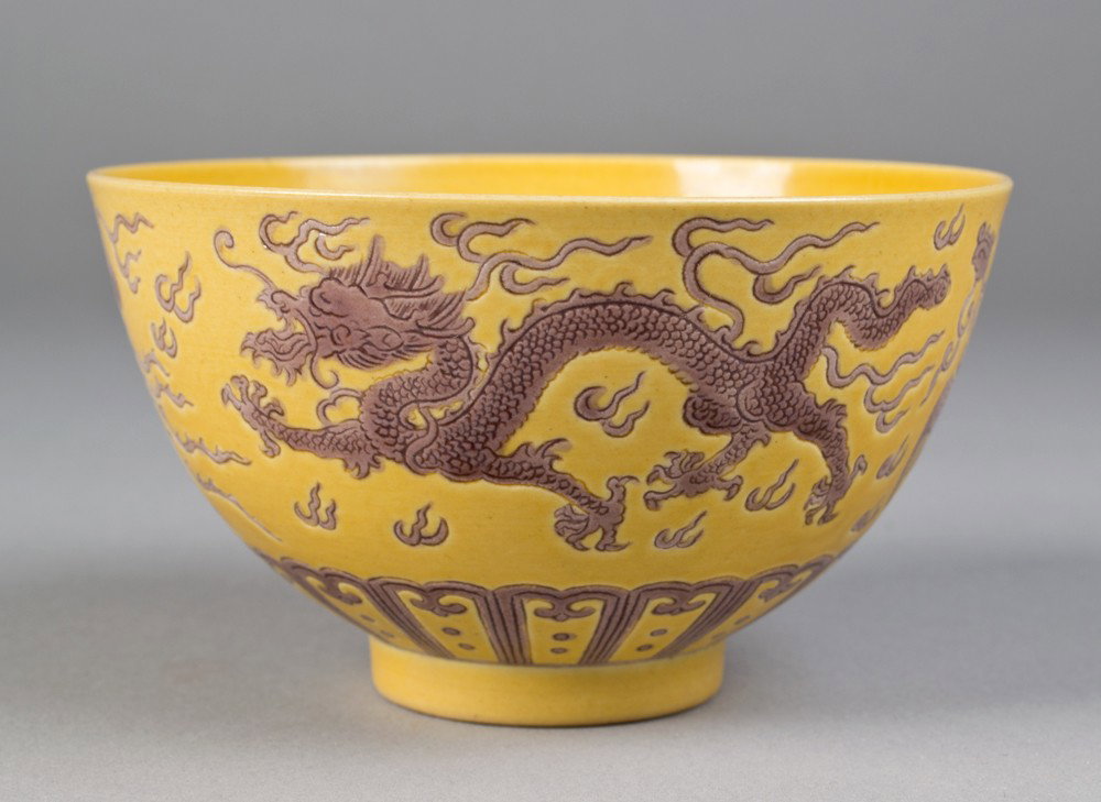 Chinese Saffron Molded Porcelain Bowl: In saffron with dragon and Phoenix in lavender chasing a flaming pearl and stiff petals at base. Six character mark for Great Qing Qianlong Production in underglaze blue on underside. 3" H x 5.25" Dia