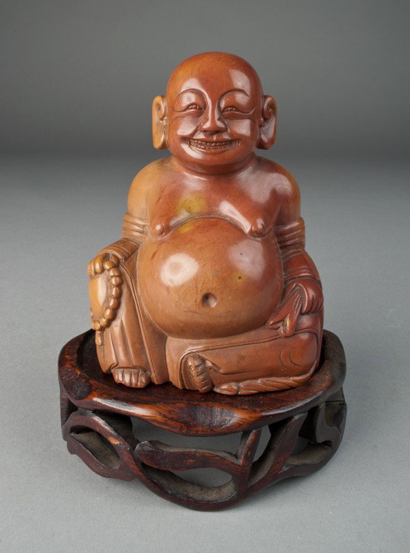 A Fine Chinese Carved Soapstone Happy Buddha: Finely carved with rosary on his knee, presented on a custom fitted openwork stand. 5.625" H including the stand. Circa late 19th/early 20th century.