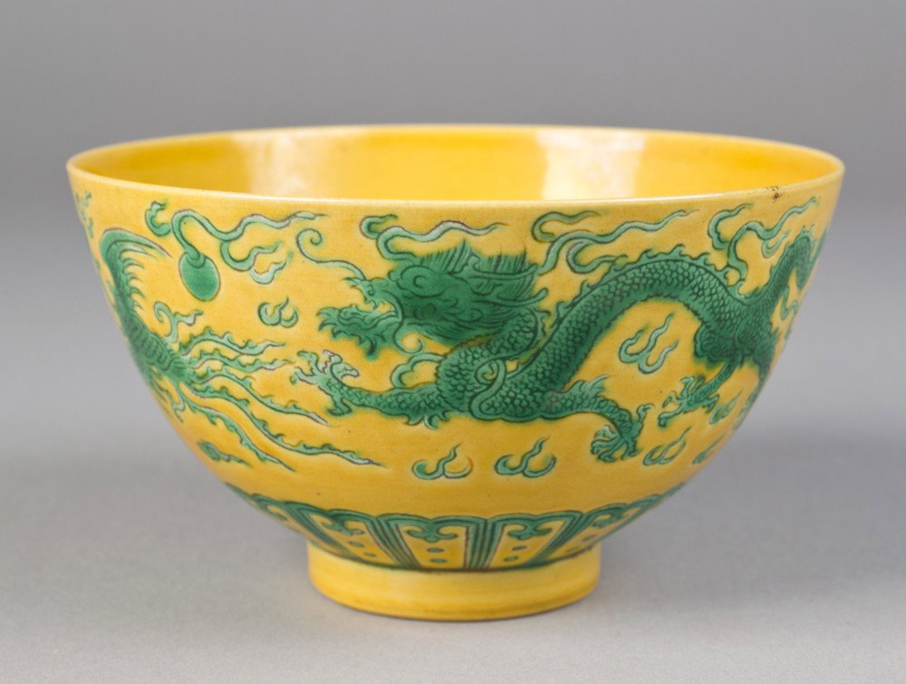 Chinese Saffron Molded Porcelain Bowl: In saffron with dragon and Phoenix in green chasing a flaming pearl and stiff petals at base. Six character mark for Great Qing Qianlong Production in underglaze blue on underside. 3" H x 5.25" Dia., 