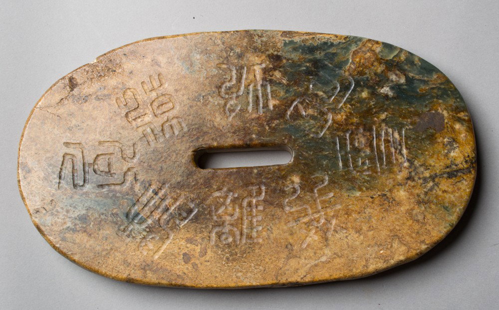 A Large Chinese Carved Soapstone Fitting: A finely carved soapstone sword fitting, carved on the front to depict symbols, the reverse with eight characters, the stone with a fine polish, 7.375"L X 4"W, circa 19th century.