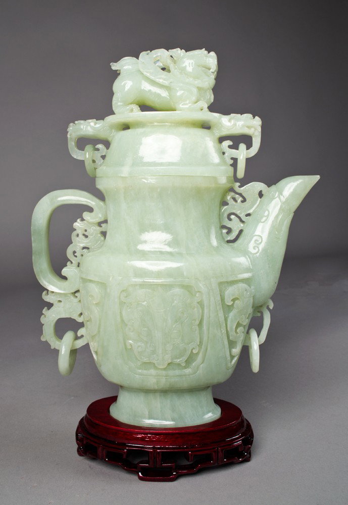 Very Fine Chinese Serpentine Jade Covered Ewer: Very finely carved depicting a bird head spout, with dragon heads, loose rings and dragon lid. On a custom wood stand and with custom fitted box. 10" H x 8" W, not including the stand. Circa 20th cent