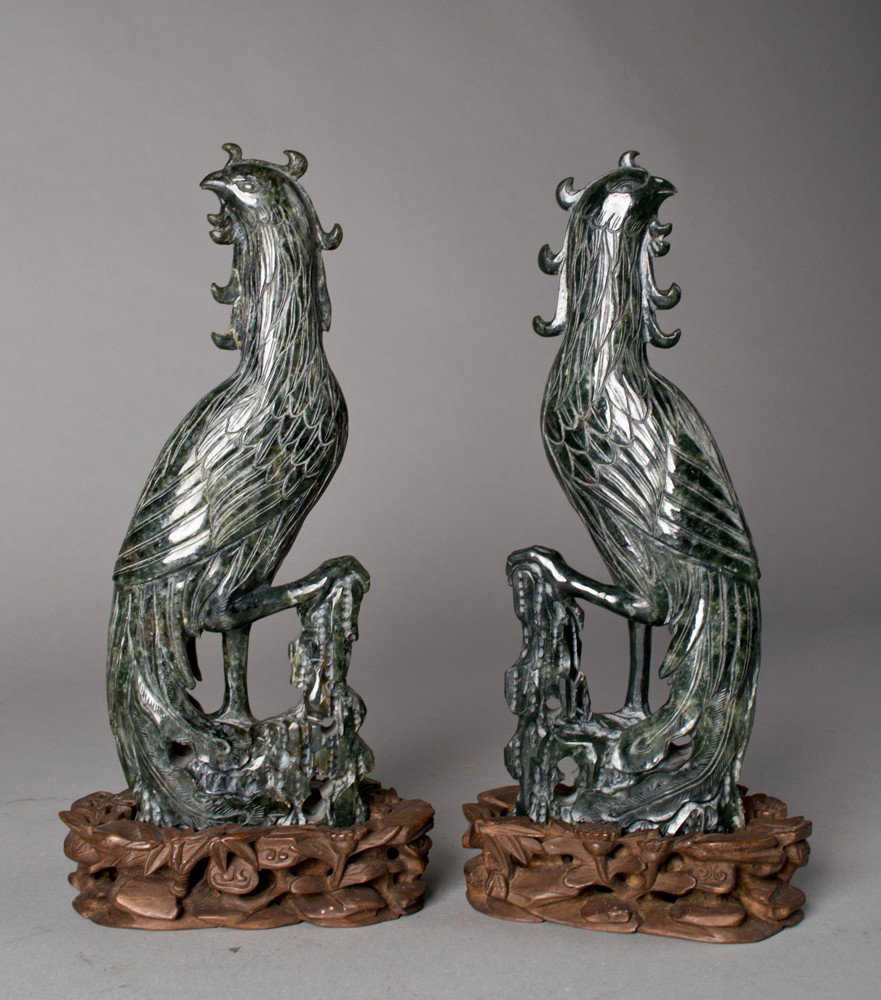 Pr. Of fine Chinese Carved Spinach Jade Birds: Both finely carved to depict a standing bird with one talon on stump both with fitted carved hardwood stands the stands finely carved to depict lingzi, 10"H each not including the stands very well don