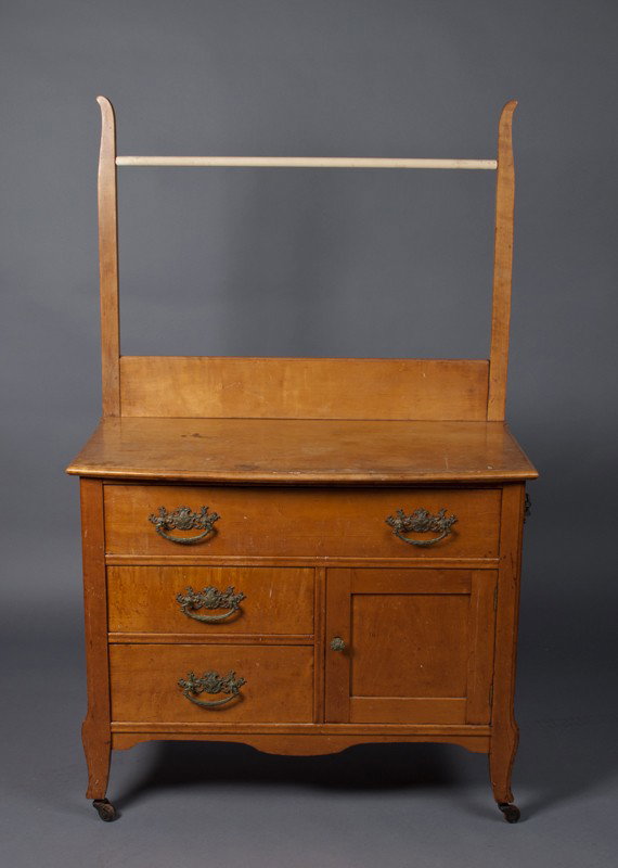 A Fine Birdseye Maple Washstand: Wheeled wash stand with three hand cut dovetailed drawers with brass pulls, single storage cupboard, overhead towel rack and towel rack on side. 51.5" H x 30.5" W x 16.25" D. Nicks and abrasions consi
