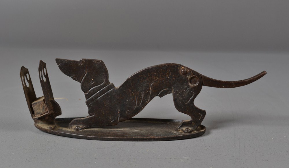 An American Art Deco Wrought Iron Cigar Cutter: Of dog form with tail that lifts for the cutter with additional match holder attached to a hammered base, 3.25"H x 10.5"L, circa early 20th century. Private collection Gregory, MI.
