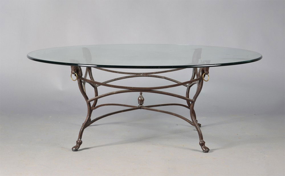 An Iron and Beveled Glass Coffee Table: Iron base with horse head terminals with loose rings, with heavy circular beveled glass top, with arched stretcher and urn form finial. 17.75" H x 48" Dia. Circa mid 20th century. Private collection M