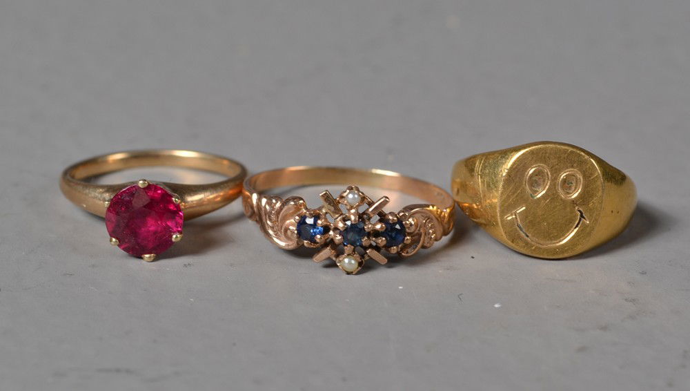 (3) 10K Gold And Gemstone Rings: To include a sapphire and seed pearl ring, prong set possible ruby and gold smile face ring, largest is 8.25, 6 grams total weight. Private collection Gregory, MI