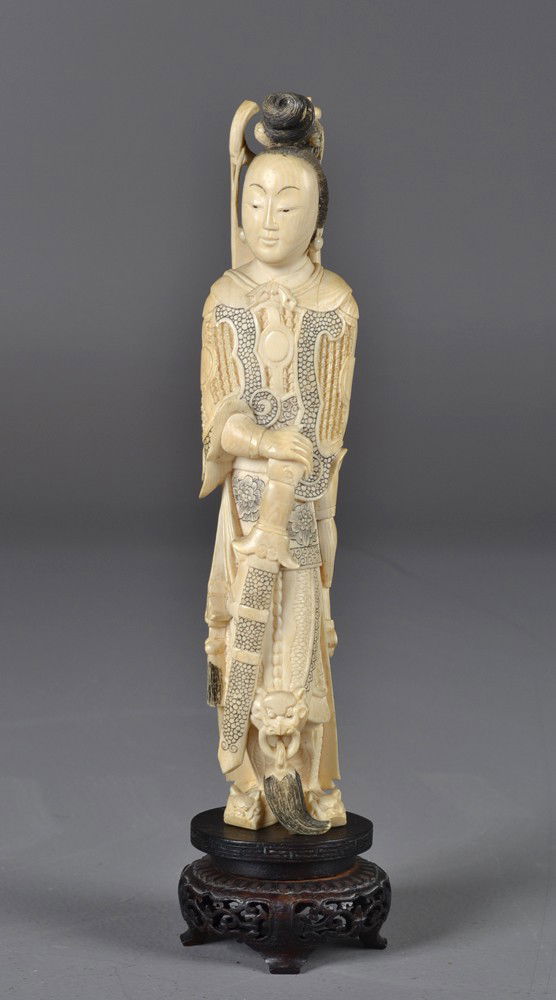 A Chinese Carved Ivory Figure of a Female Warrior: Finely carved to depict a female warrior with sword, bow and arrows on her back and breast armor, on fitted carved hardwood stand with openwork carving, 11.5"H including the stand, circa late 19th/ear