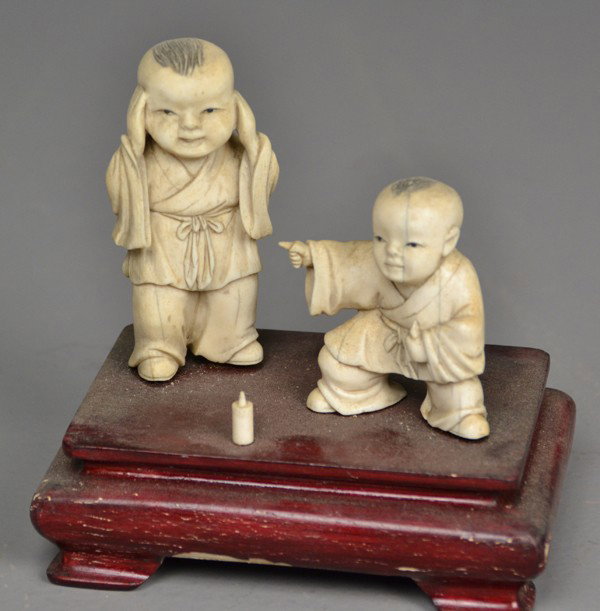 Chinese Cultural Revolution Ivory Carving: Finely carved to depict two mischievous young boys and what we believe to be a candle or perhaps a bottle, both with inked and dyed elements, both attached to carved hardwood stand, tallest measures 3