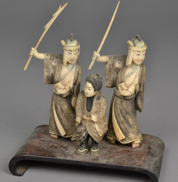 A Fine Japanese Ivory Okimono Group: Probably Meji period, finely carved to depict three figures, one woman and two men on a silver inlaid rosewood stand, very well executed detail, the men holding weapons, figures appear to be in some s