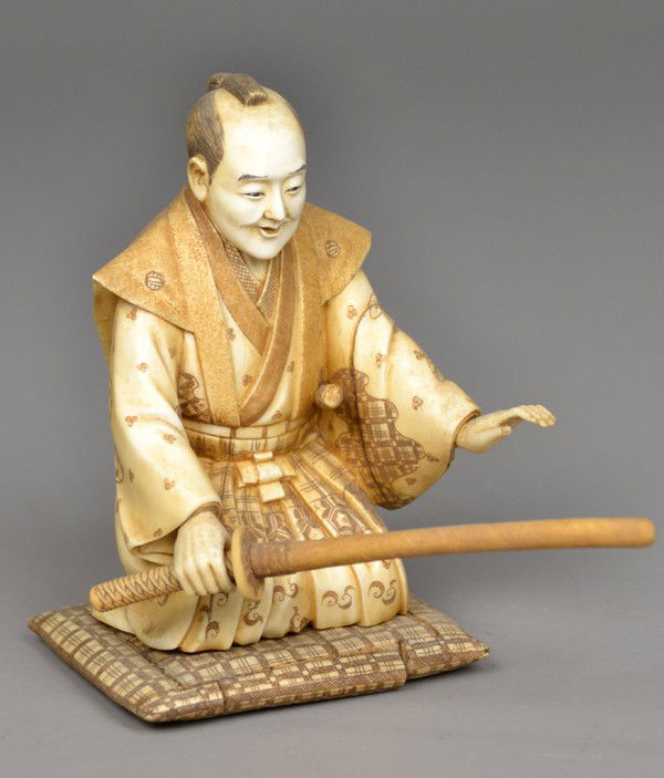 Japanese Carved Ivory Okimono Samurai: Probably Meji period, finely carved to depict a samurai warrior knelling on a mat holding a removable katana, with inked and dyed elements, very remarable, measures 5" H. Private collection Oxford MI.