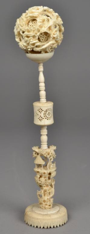 Chinese Qing Ivory Puzzle Ball On Stand: Finely carved with multiple layers the outside layer depicting dragons, the stand carved to depict a traditional village scene with figures moving down a reticulated stair case, measures 12" H, circa 
