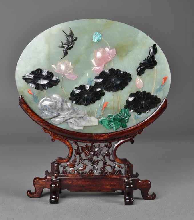 Chinese Qing Jade & Hardstone Plaque on Stand: A finely-carved light green jade oval plaque inlaid with jade rose quartz, malicite, soapstone, and red coral depicting lotus blossoms, lilies, and magpies on fitted carved openwork stand with six ruy