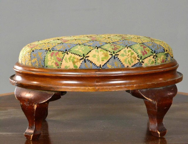 An Early American Empire Mahogany Foot Stool: A petite oval foot stool in mahogany, with checkerboard needlepoint seat raised on cabriole legs with block feet, retains its original surface with a fine mellow patina, the body of the foot stool is