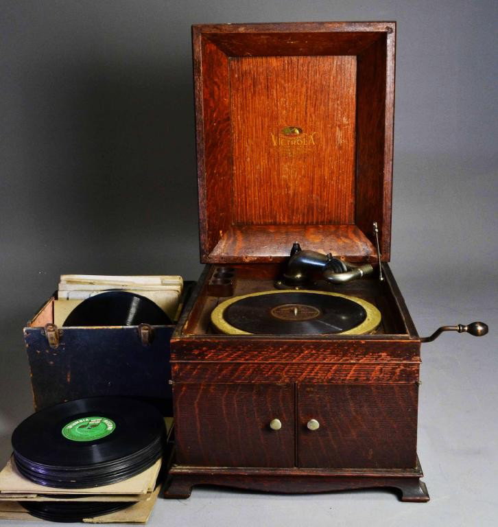 VICTROLA TALKING MACHINE & RECORDS: Table top Victrola, with box of approx. (100) mostly German old recordings. 15" H x 15.5" W X 20" L. Early 20th century. Condition issues: cover needs to be fastened, some minor scratches, and paint s
