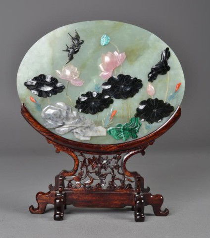 Chinese Jade & Hardstone Plaque on Stand: Afinely carved oval plaque inlaid with jade rose quartz, malicite, soapstone, and red coral depicting lotus blossoms, lilies, and magpies on fitted carved openwork stand with six ruyi shaped feet, 14"