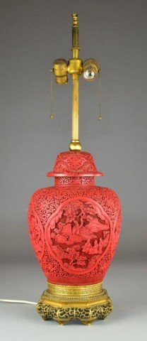 Chinese Carved Cinnabar Vase And Cover: Finely carved with four panels depictin figuers in landscapes with ancenit pines, the balance carved to depict lotus blossoms and tendrils, now mounted as a lamp with gilt bronze vase, cinnabar measur