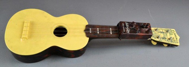 Emenee Flamingo Plastic Soprano Ukulele: An Arthur Godfrey signed, yellow and marbleised brown, the headstock features an image of hula girls and palm trees, this is not a toy but a working instrument, with six chord buttons, nice clear soun