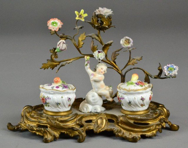 A Fine French Gilt Bronze & Porcelain Ink Stand: In the Rococo taste, modeled in the form of a tree with hand painted porcelain rosettes, the ink pots shaped as covered pots, centered by a porcelain putto, 10.5" W x 7.75" H, circa late 19th century.