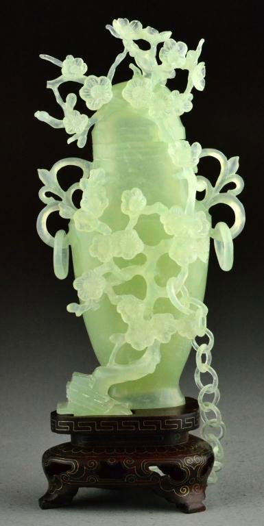 Chinese Qing Celedon Jade Vase And Cover: A finely carved vase and matching cover; depicting lotus blossoms and tendrils; hung with loose rings and chain; raised on silver inlaid stand; 6.5"H not including the stand; circa late19th-early 20th