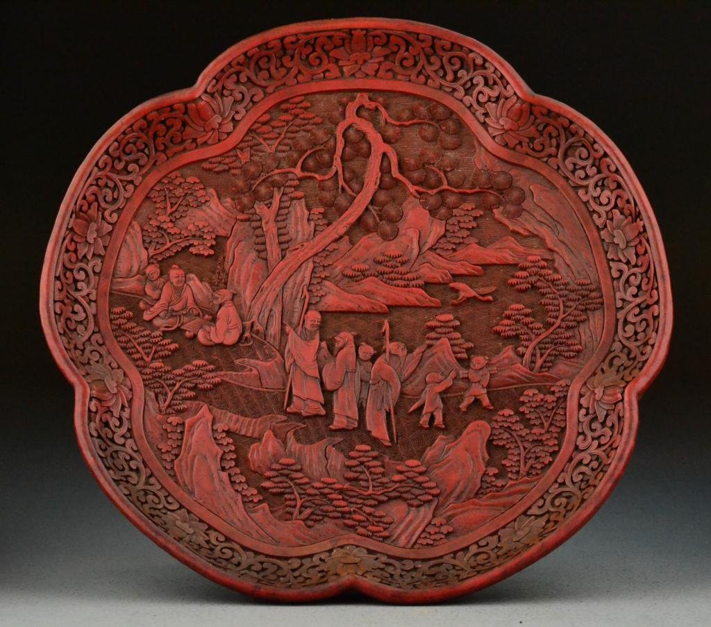 Chinese Qing Carved Cinnabar Lotus Plate: Very finely carved in the shape of a lotus flower to depict figures within a landscape, bordered with carved lotus blossom and scrolling symbols, 1.75"H X 12.5"D, circa late 19th/early 20th century. I
