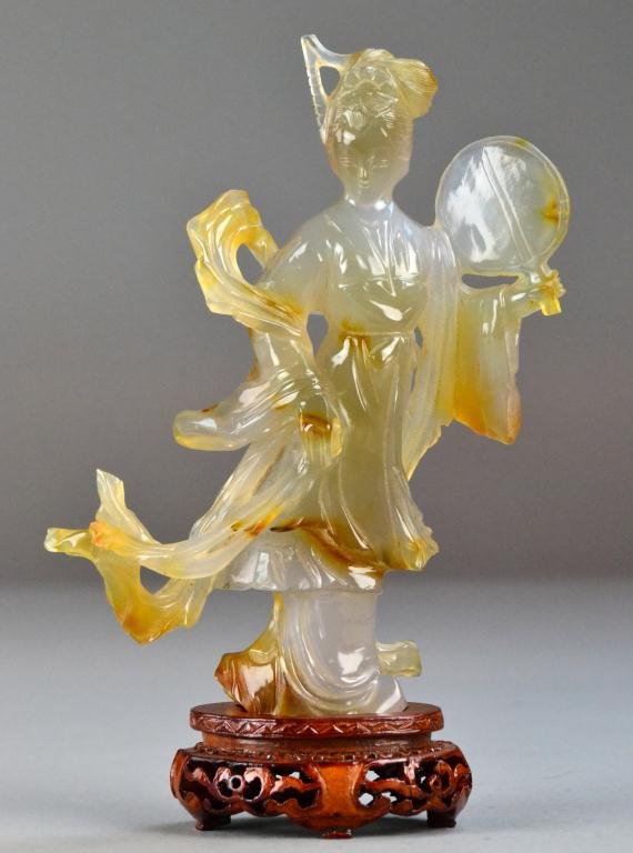 Chinese Qing Carved Agate Guan Yin: Finely carved, one hand holding a mirror the other her robe, the stone with good color with areas of russet skin and very good polish, raised on hardwood stand with open work carving, 7"H, not includi