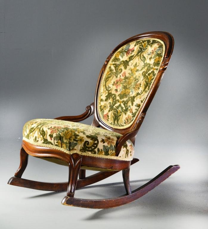 An American Antique Fireside Rocking Chair: Carved walnut fireside rocker with floral upholstered back and seat, scalloped apron and carved legs. 32" H, circa late 19th early 20th century. Light wear to back legs of rocker, otherwise good condi