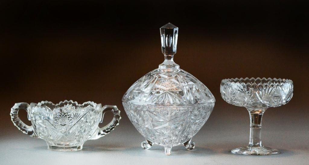 (3) Pieces American Brilliant Cut Glass: To include a footed compot, a two handle open sugar bowl, and a covered dish raised on tripod feet, tallest is 8.5" H. Circa early 20th century.