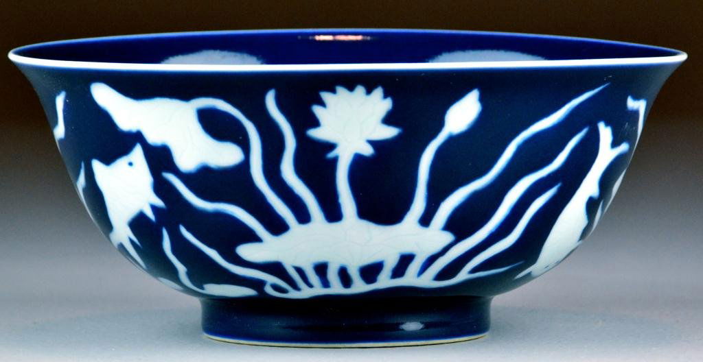Chinese Large Blue Bowl with White Flowers: Dark blue porcelain bowl with white silhouettes of fish and lotus plants and white lotus plant in center of bowl surrounded by one white circle, underglazed symbols inside two concentric blue circles,