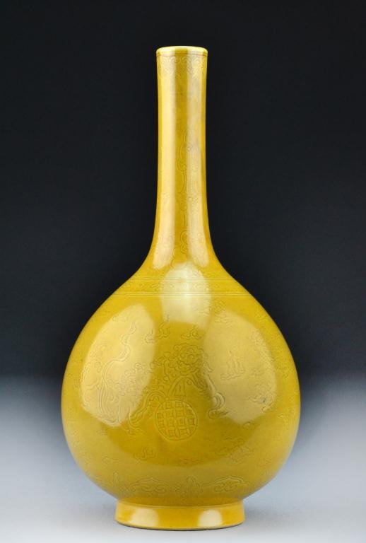 Chinese Mustard Yellow Porcelain Vase: The elongated bottle form mustard yellow vase having incised decoration depicting foo lions plaing with balls among ruyi clouds, raised on short foot ring, the base bearing Qianlong seal mark in black