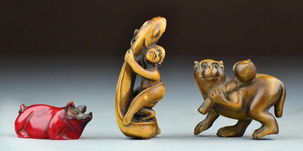(3) Japanese Carved Netsuke: To include two carved wood examples, one to depict a monkey holding branch with peaches and one carved to depict a man clinging to a snake, together with an amber example carved to depict a pig, all t