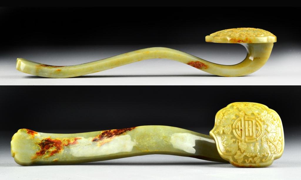 Chinese Qing Carved Jade Ruyi Sceptor: The shaped head carved to depict bats surrounding a shou symbol, the stone a celedon with russet patches, very well executed with finely carved details and a wonderfull polish. 14.625"L, circa 19th ce