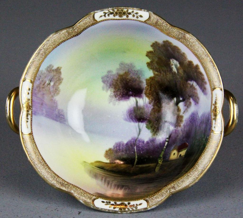 A Fine Noritake Porcelain Scenic Bowl: Finely painted to depict landscape with cabin trimmed in gilt with two handles, bearing the green-leaf Noritake mark, 7" Diameter x 2.25" H, circa early 20th century. Provenance: private collection of