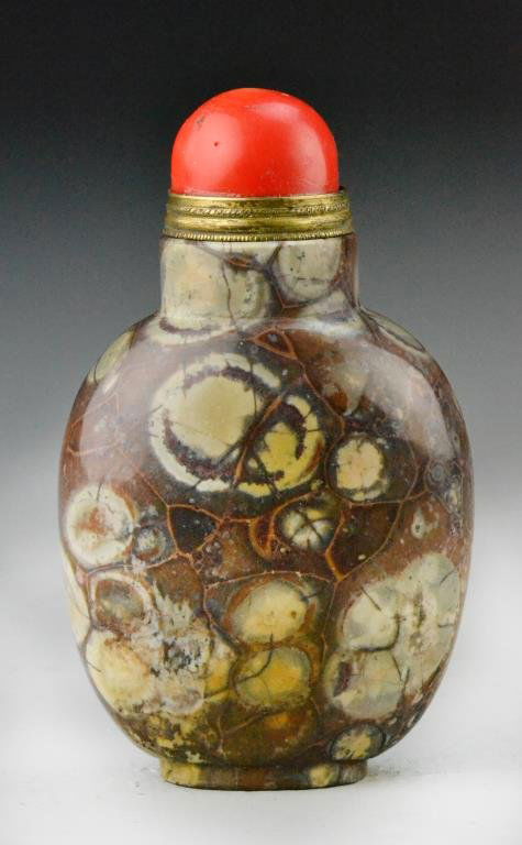 Chinese Pudding Stone Snuff Bottle: Exceptional pudding stone snuff bottle in flattened round shape sitting on an oval raised foot, well hollowed with a red coral stop and brass spoon, 3.5"H, circa late 19th/early 20th century. Private