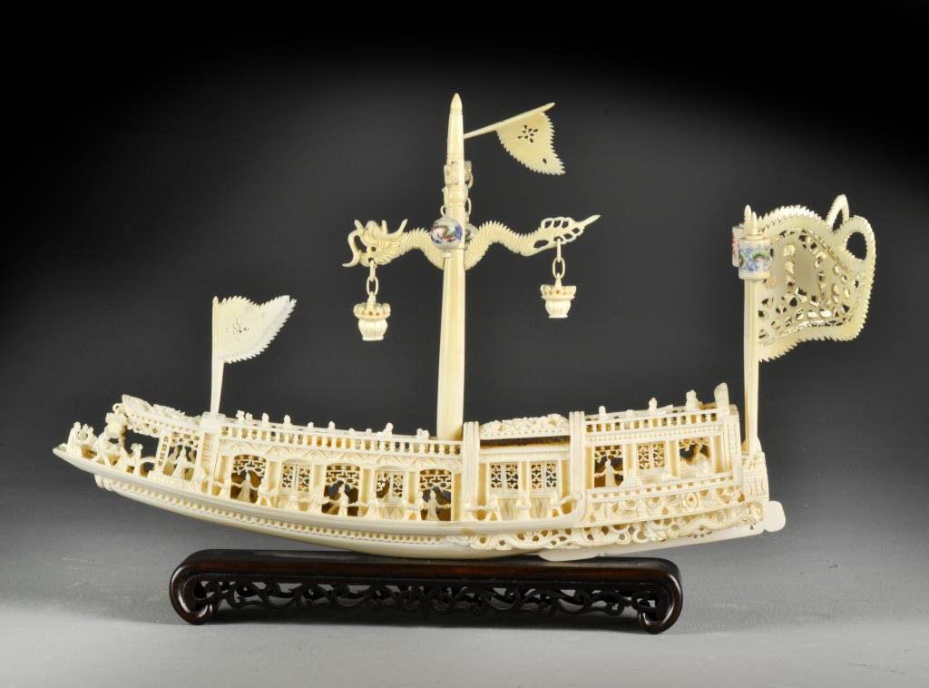 Chinese Polychrome Painted Ivory Junk: Finely and intricately carved to depict a Chinese junk ship with many figures, having five flags and having lanterns polychrome painted, raised up on hardwood stand, 10.5"H X 16"L including stand, cir